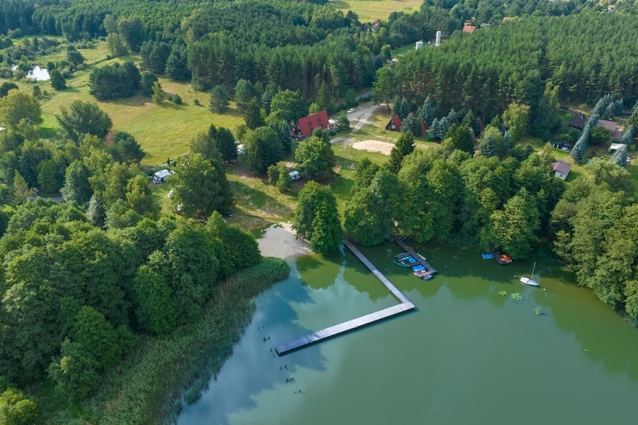 Jezioro z pomostem i piaszczystą plażą wśród drzew, widok z lotu ptaka
