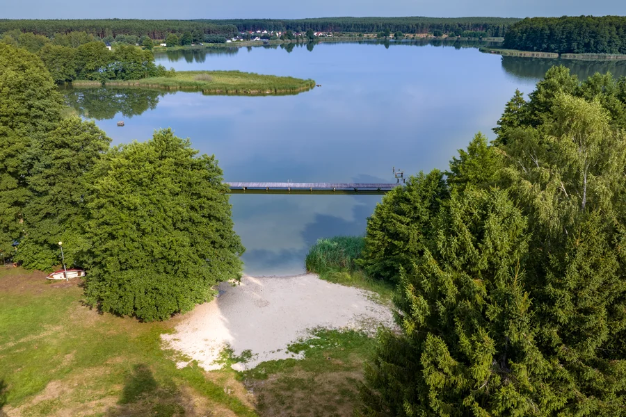 Jezioro między lasami z kładką i piaszczystym brzegiem, widok z lotu ptaka