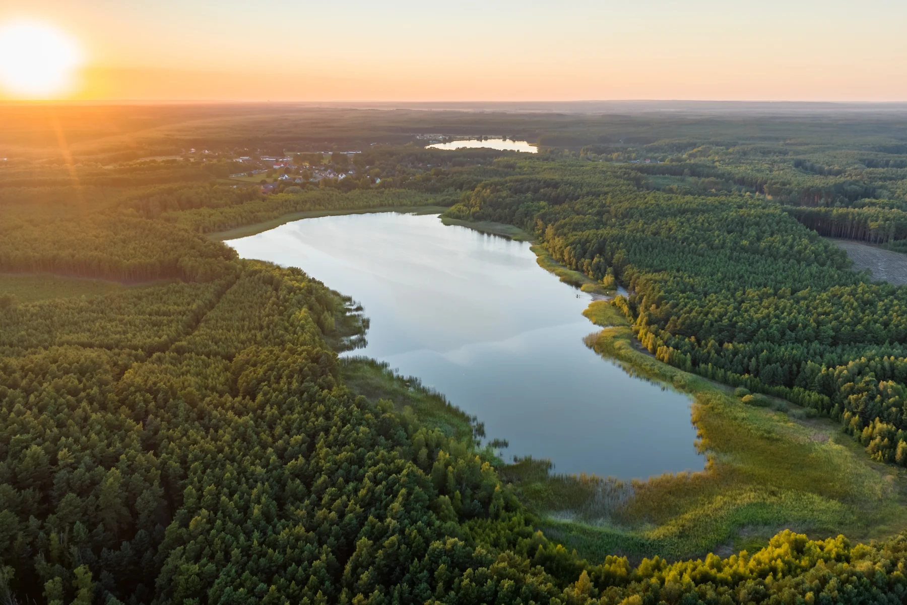 Jezioro w rozległym kompleksie leśnym, słońce nisko nad horyzontem, widok z lotu ptaka